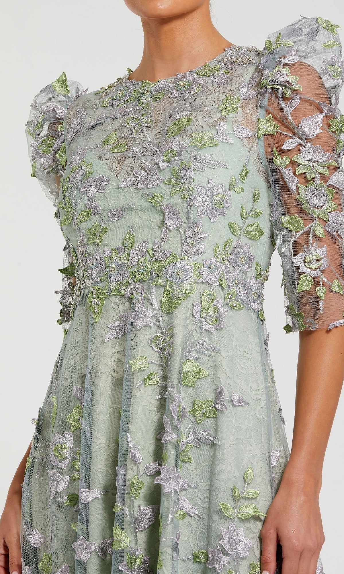 A woman wears the Mac Duggal 68193 Tea-Length Lace Formal Dress in light green, featuring floral appliqué and sheer puff sleeves, shown from shoulders to mid-thigh.